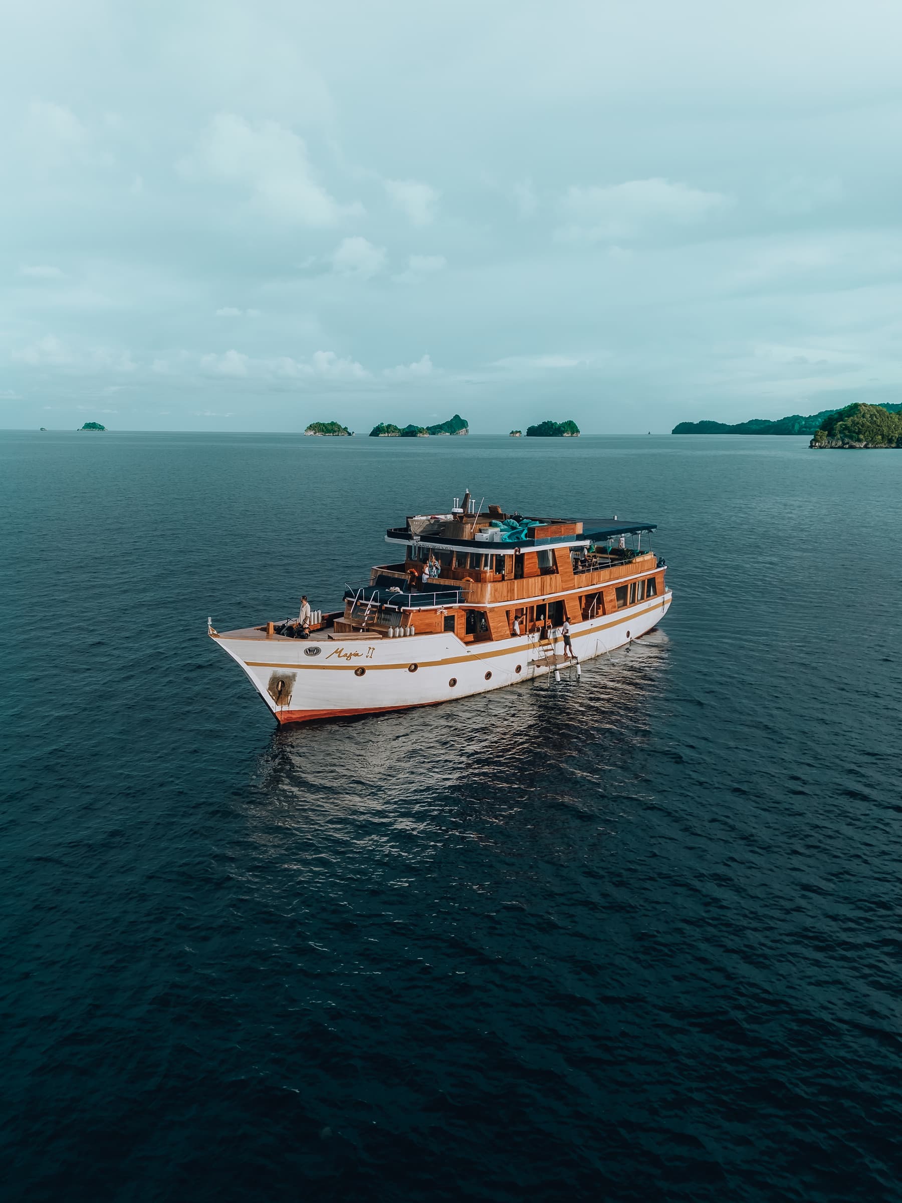 Aerial view of the liveaboard Magia 2 anchored on calm water with small islands on the horizon