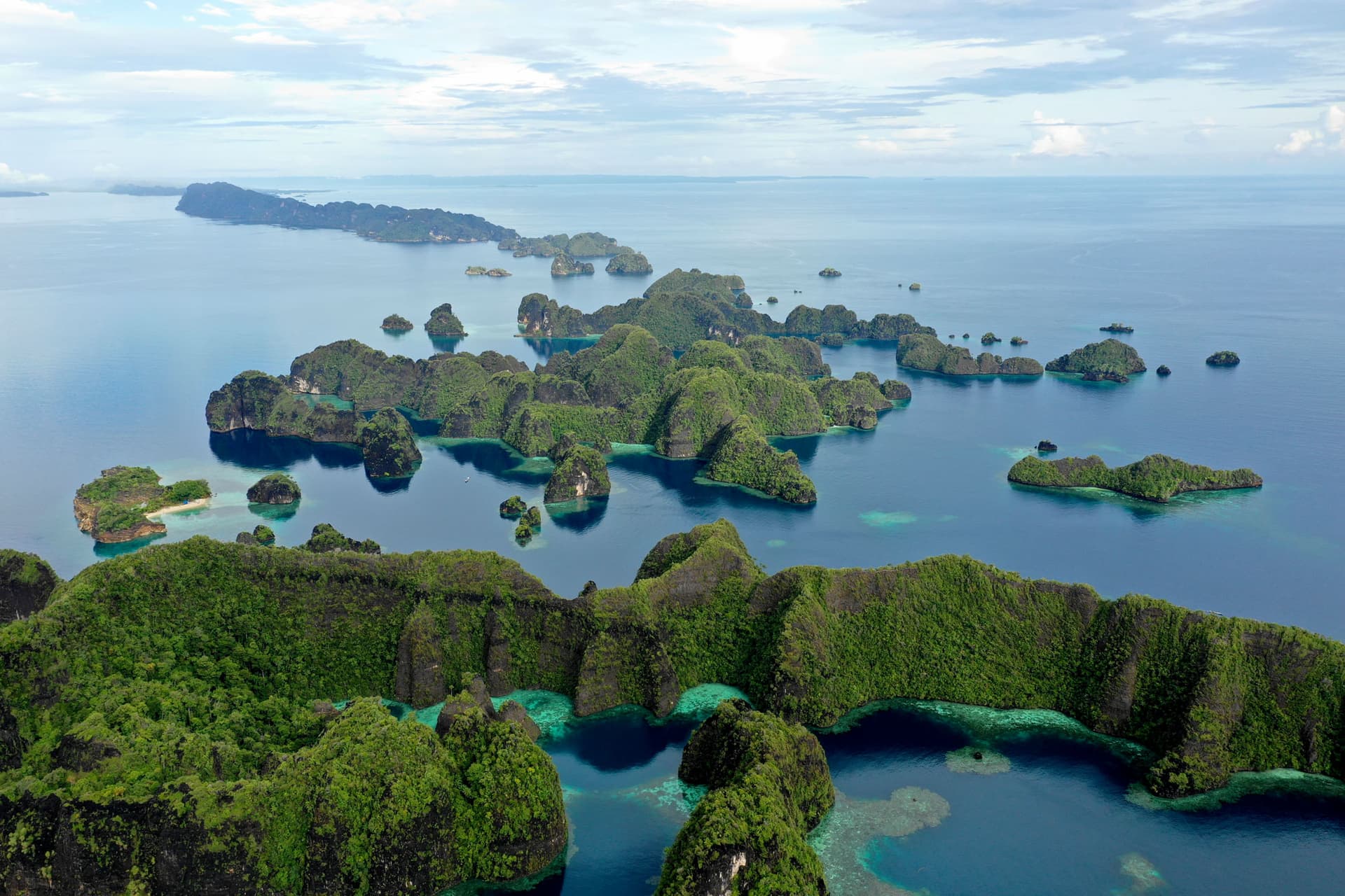 Aerial view of small forested limestone islands scattered across a calm blue lagoon with turquoise shallows