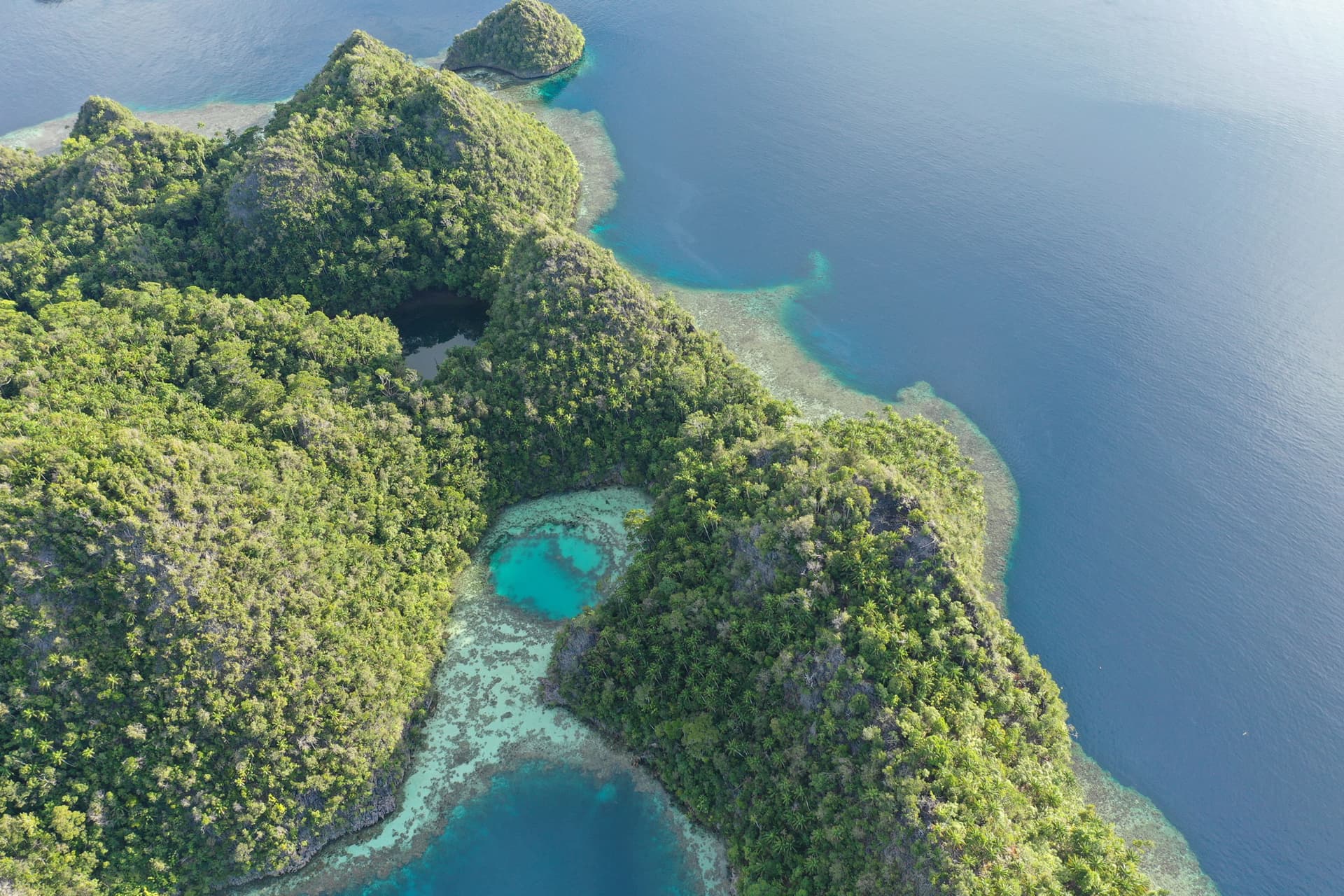 Aerial view of forested limestone islands with hidden turquoise lagoons connected to the surrounding blue sea