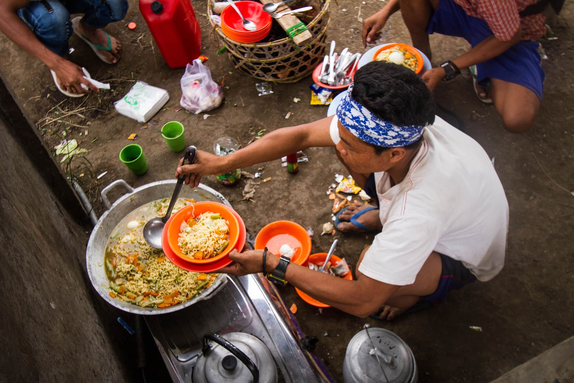 Overhead view of a street vendor serving fried noodles from a large wok into an orange bowl