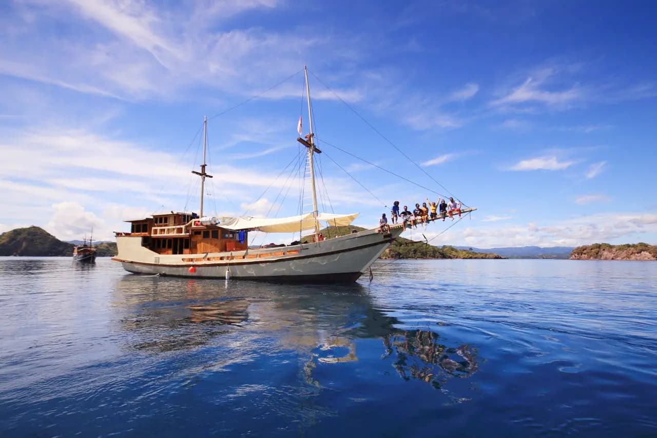 The Lalunia liveaboard anchored on calm water with guests gathered on its bow platform under a blue sky
