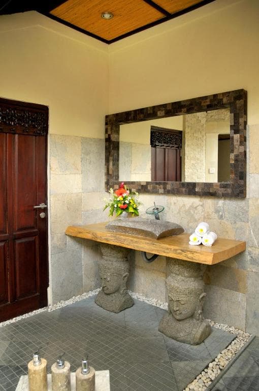 Bathroom at Hidden Paradise with stone head pedestals supporting a wooden sink, framed mirror, and decorative flowers and towels
