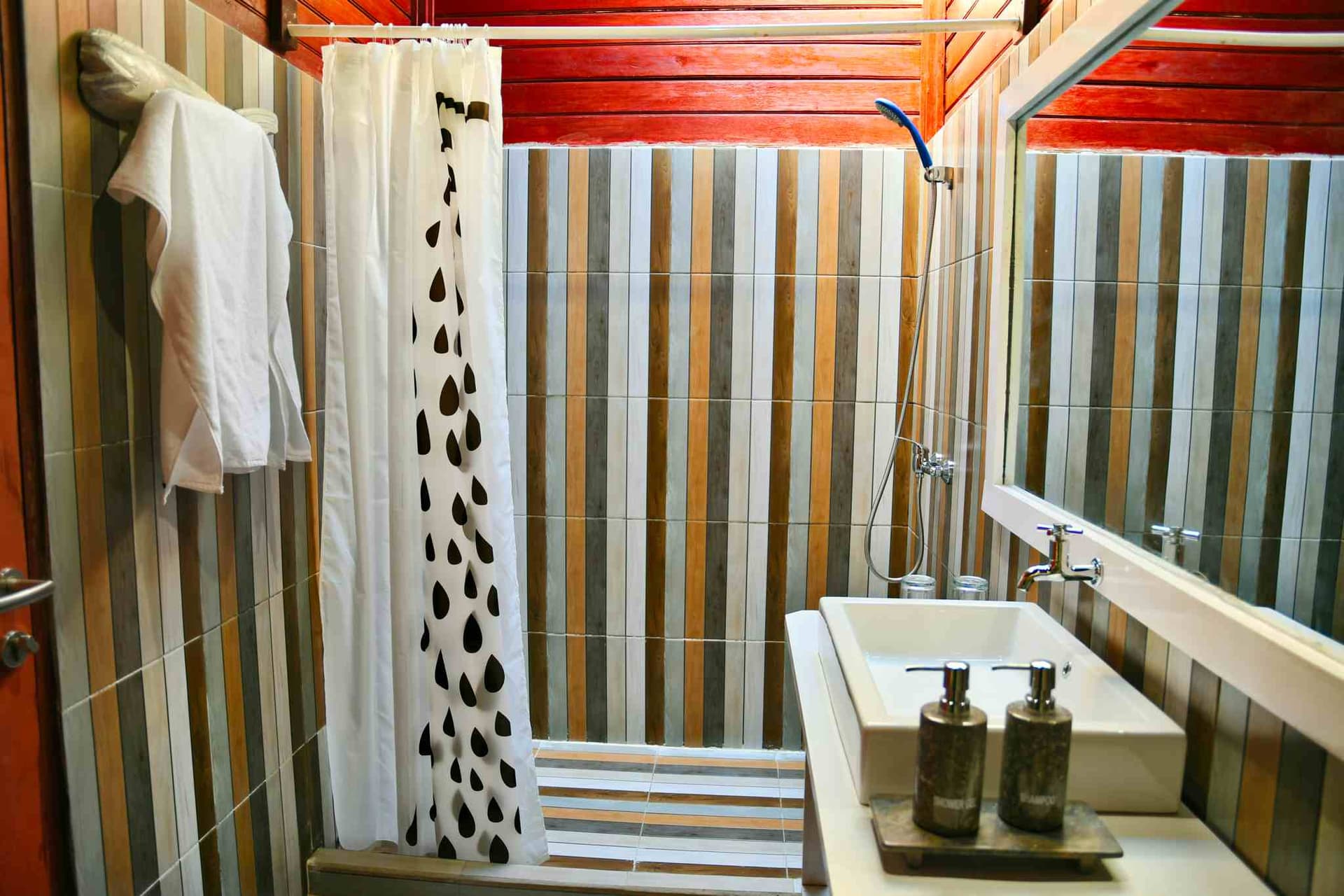 Cove Eco Resort bathroom with striped tile walls, sink with soap dispensers, shower area with patterned curtain, and towels