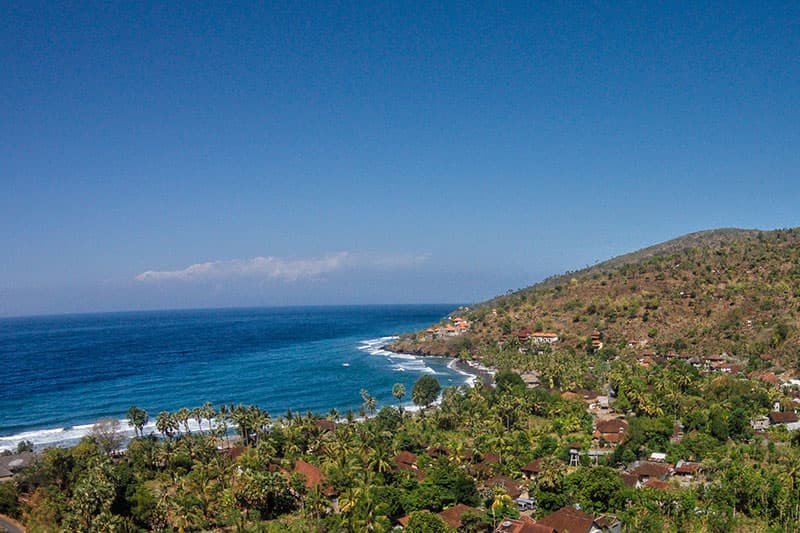 Aerial view of a coastal village with red-roofed buildings and palm trees along a curved bay