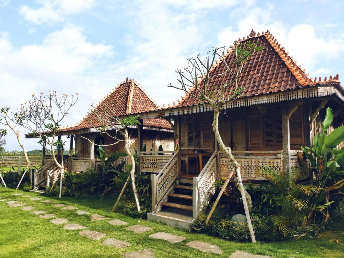 Aswanaya Villa's traditional wooden buildings with tiered roofs, decorative railings, and tropical plants on manicured grounds under blue sky