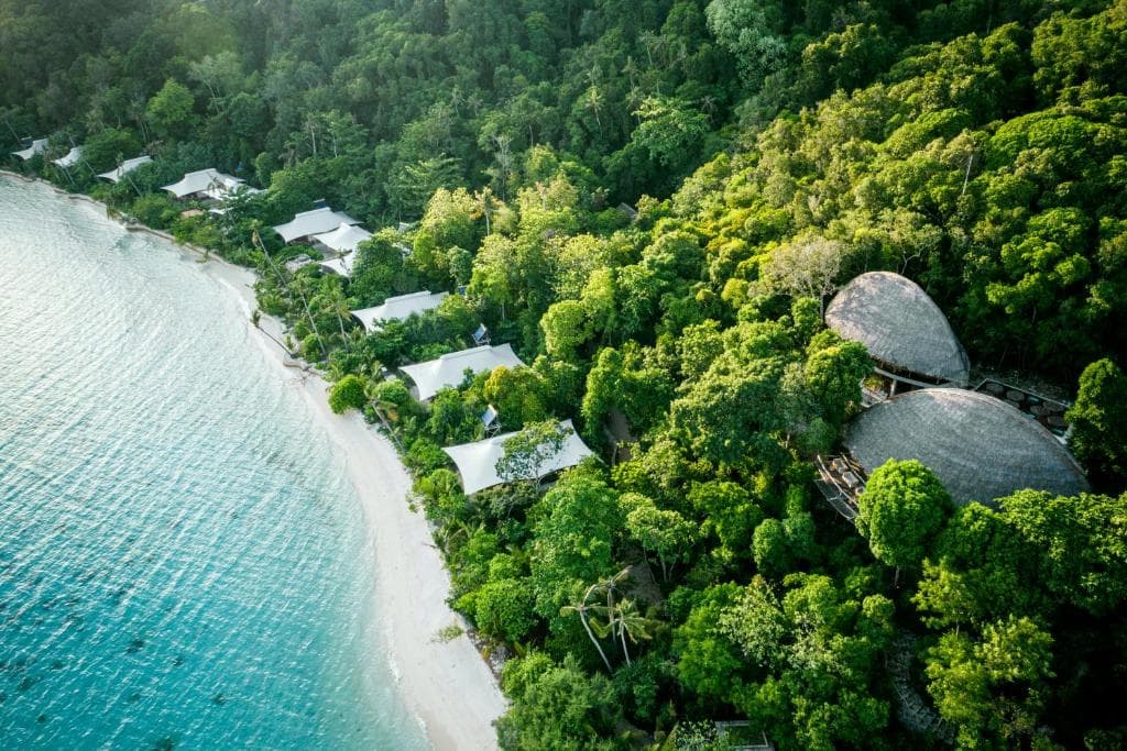 Aerial view of Bawah Reserve Riau showing white-roofed accommodations nestled among dense tropical forest along a turquoise shoreline