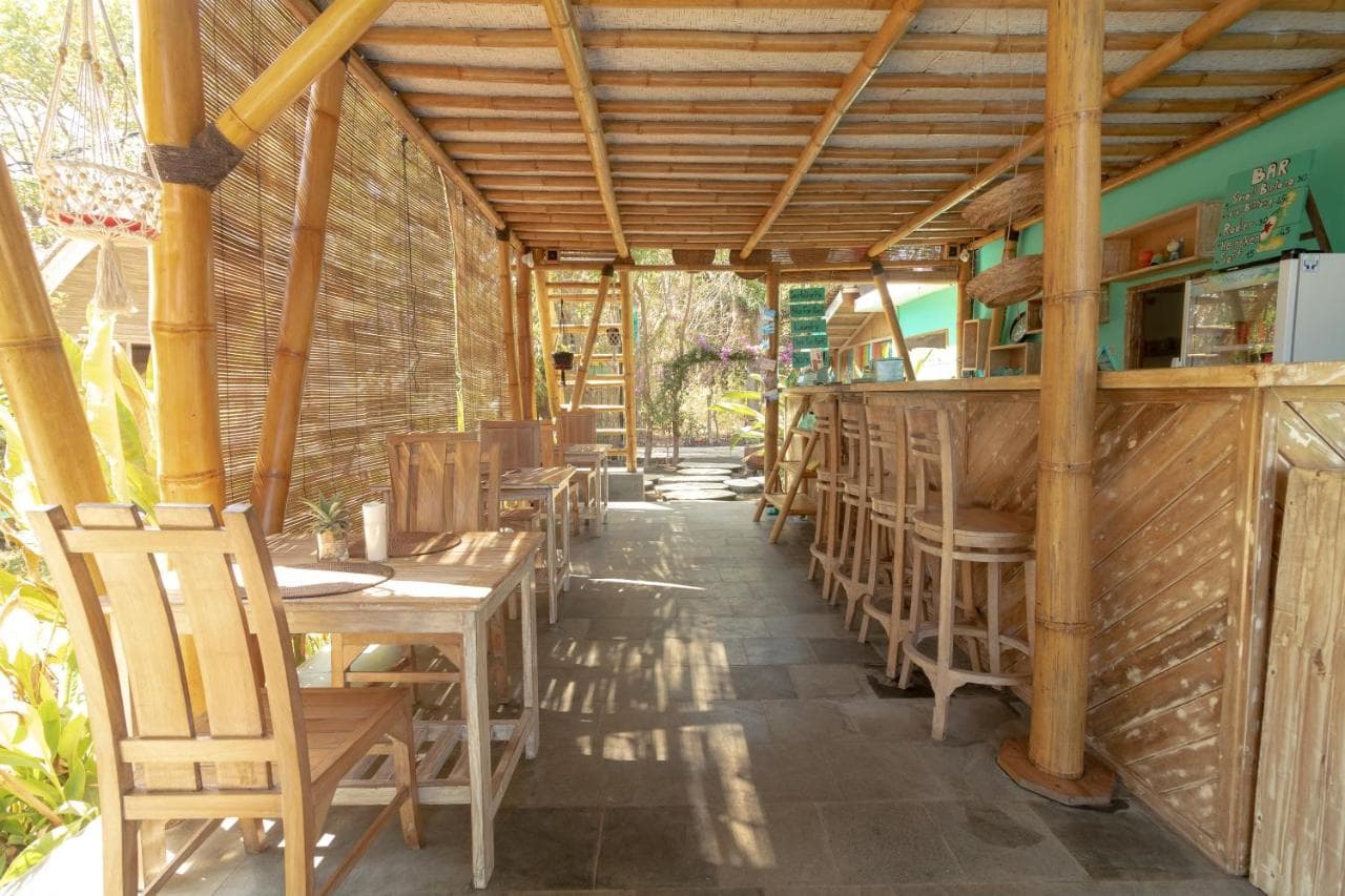 Covered wooden restaurant or bar area at Gili Matiki with wooden chairs, tables, and woven walls, with a service counter visible in the background