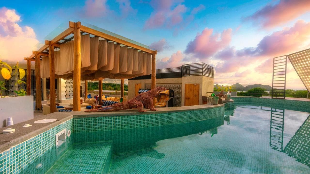 Loccal Collection Hotel's poolside area at sunset, with a wooden pergola structure, tiled pool, and seating areas overlooking landscaped grounds