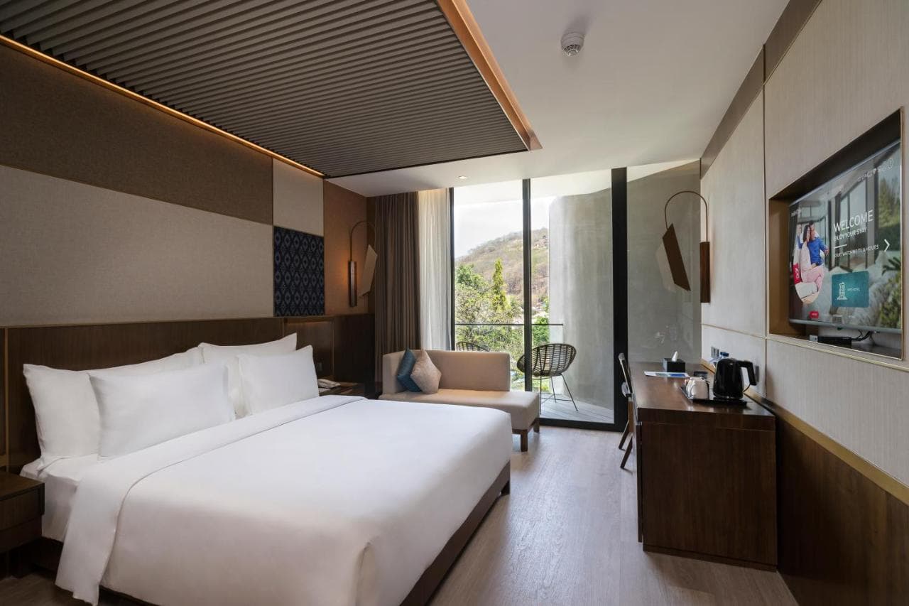 Modern hotel room with queen bed, sitting area, desk, television, and floor-to-ceiling windows with a view outside