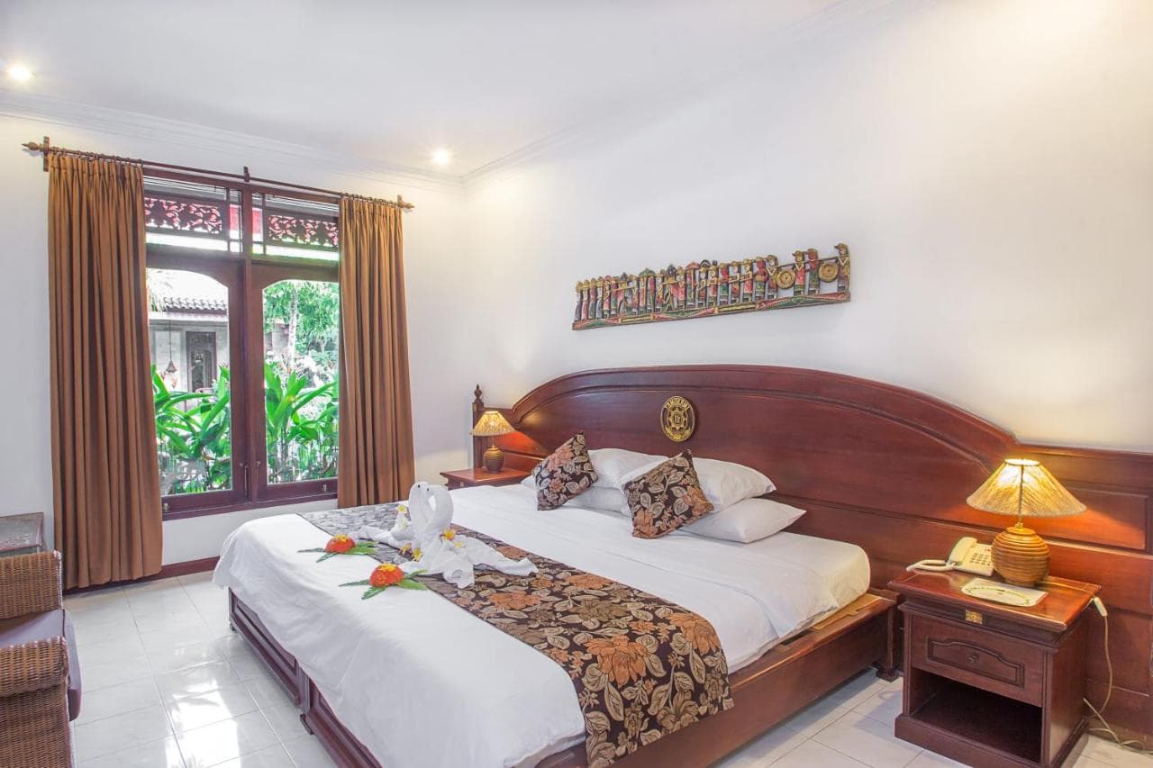 Tamukami Hotel bedroom with wooden bed, white linens, decorative pillows, twin bedside lamps, wooden doors opening to garden view, and wall art