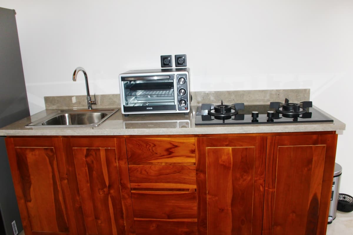 Kitchen counter with wooden cabinets, stainless steel sink with faucet, gas cooktop, small oven, and marble countertop at Villa Bulan Bali