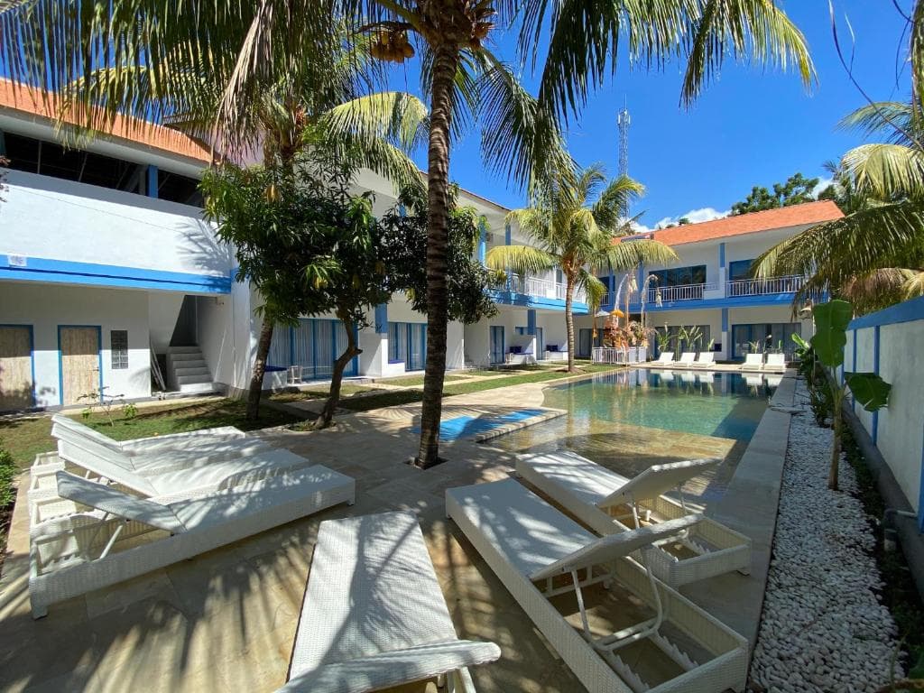 Kura Kura Divers Lodge courtyard with loungers, palm trees, white buildings with blue trim, and a central pool or water feature