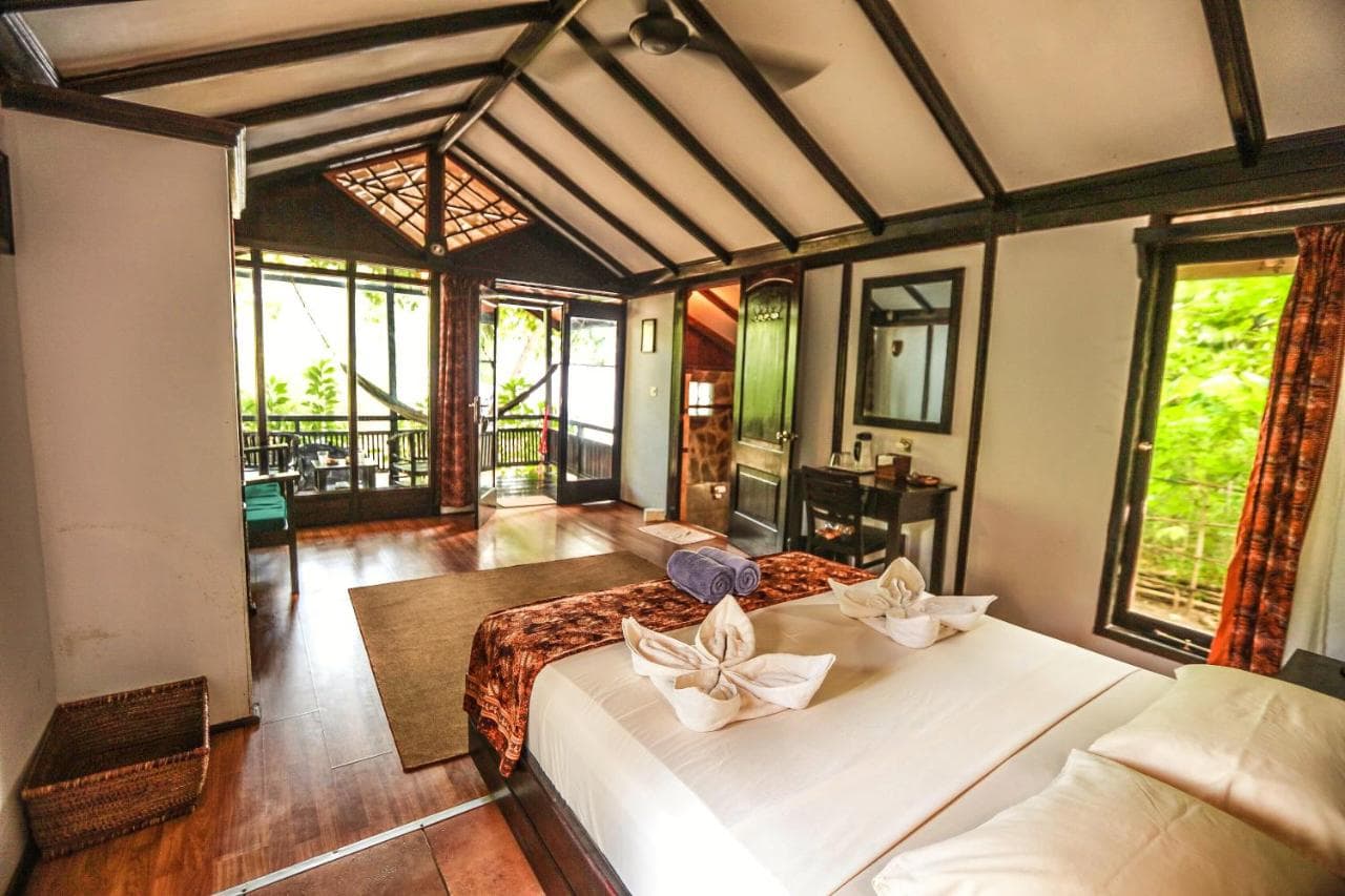 The Village Bunaken spacious bedroom with two beds, wooden flooring, vaulted ceiling with skylights, and glass doors opening to outdoor areas