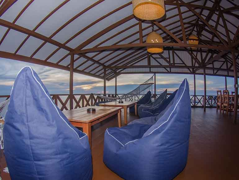 Blue bean bag seating on a covered wooden deck with dining table, pendant lights, and a view outside
