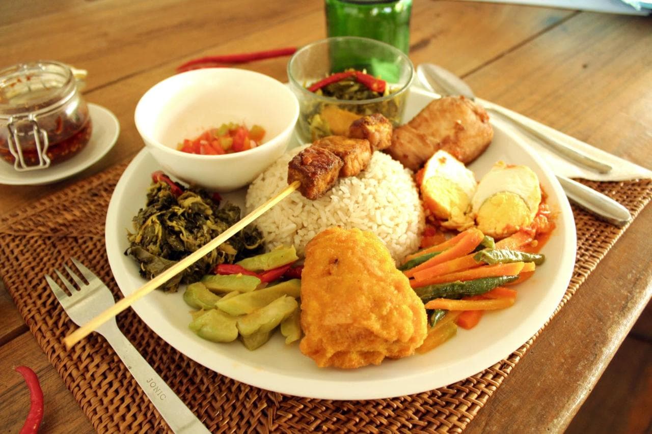 A plated meal at Coral Eye featuring rice, fried items, vegetables, and side dishes with condiments and chopsticks on a wooden table