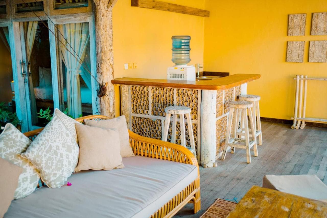 Les Villas Ottalia common area with yellow walls, wooden bar with woven panels, bar seating, a daybed with cushions, and blue-shuttered doors