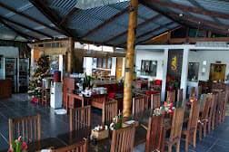 NAD Lembeh's open-air dining and lounge area with wooden furniture, central support post, and corrugated metal roof