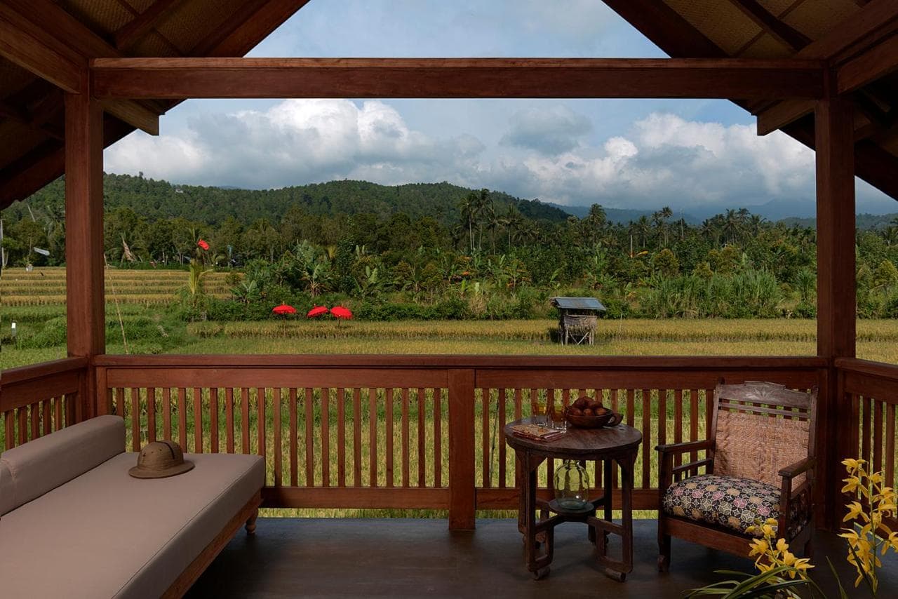 Wooden pavilion with seating and small table overlooking rice paddies, forested hills, and cloudy sky