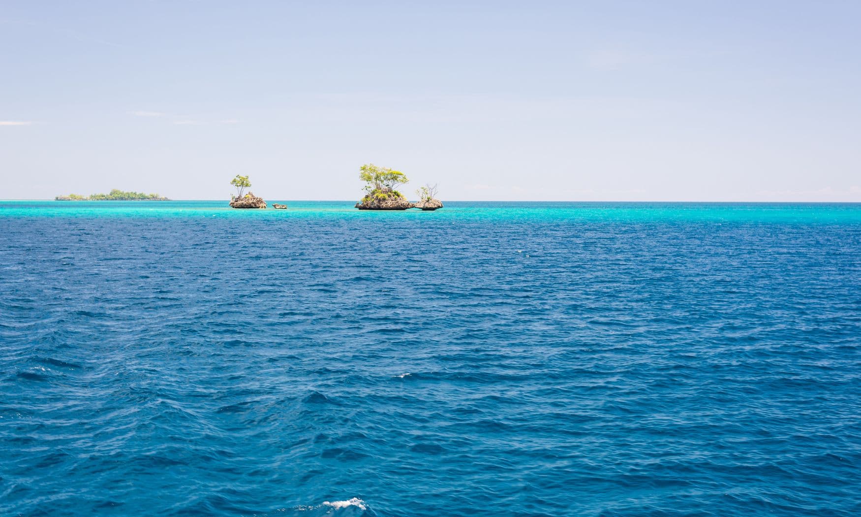 Small tree-covered limestone islets rising from turquoise shallows, with deep blue open water in the foreground