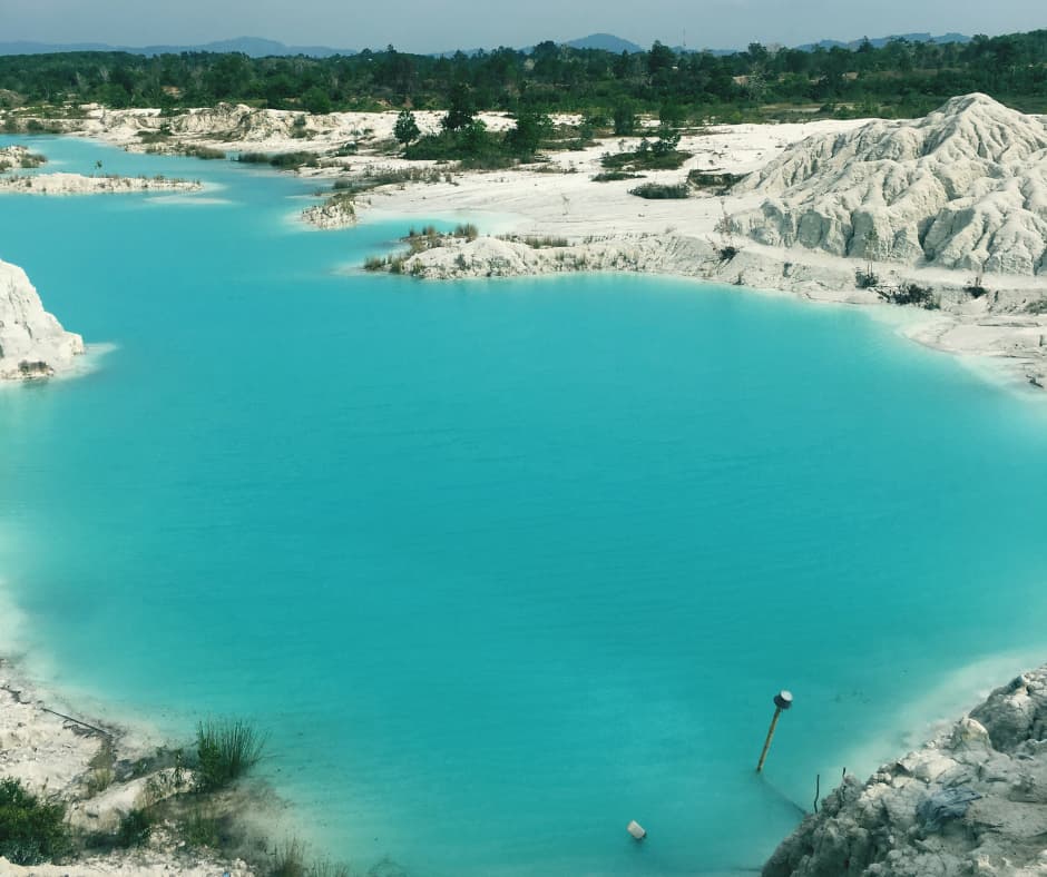 Turquoise lake surrounded by white chalky cliffs and sand, with green trees and hills in the distance