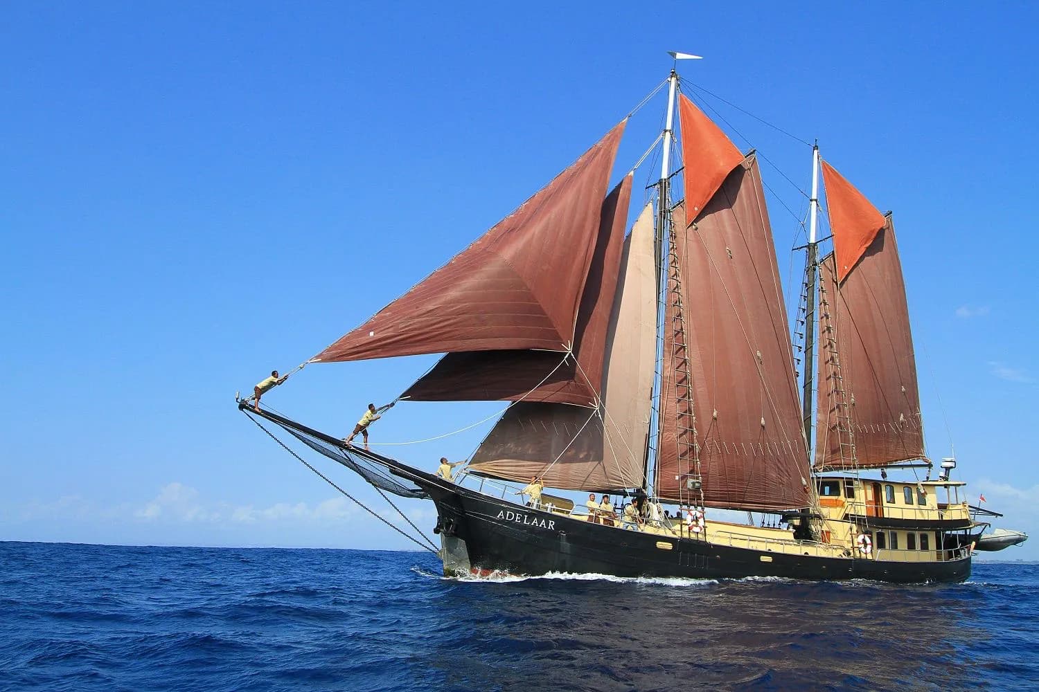 The traditional sailing vessel Adelaar with rust-colored sails raised, crew members standing on the bow rigging, sailing on open water