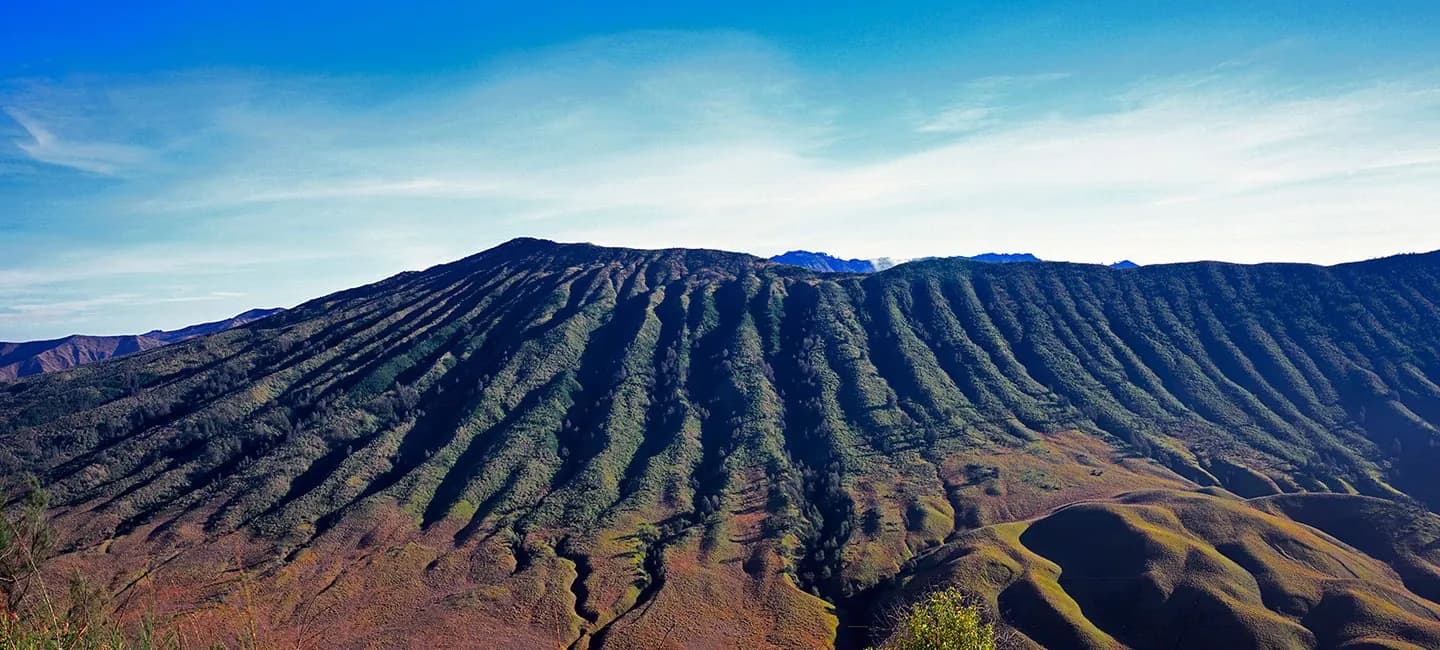 Aerial view of deeply eroded volcanic terrain with parallel ridges and ravines under clear blue sky