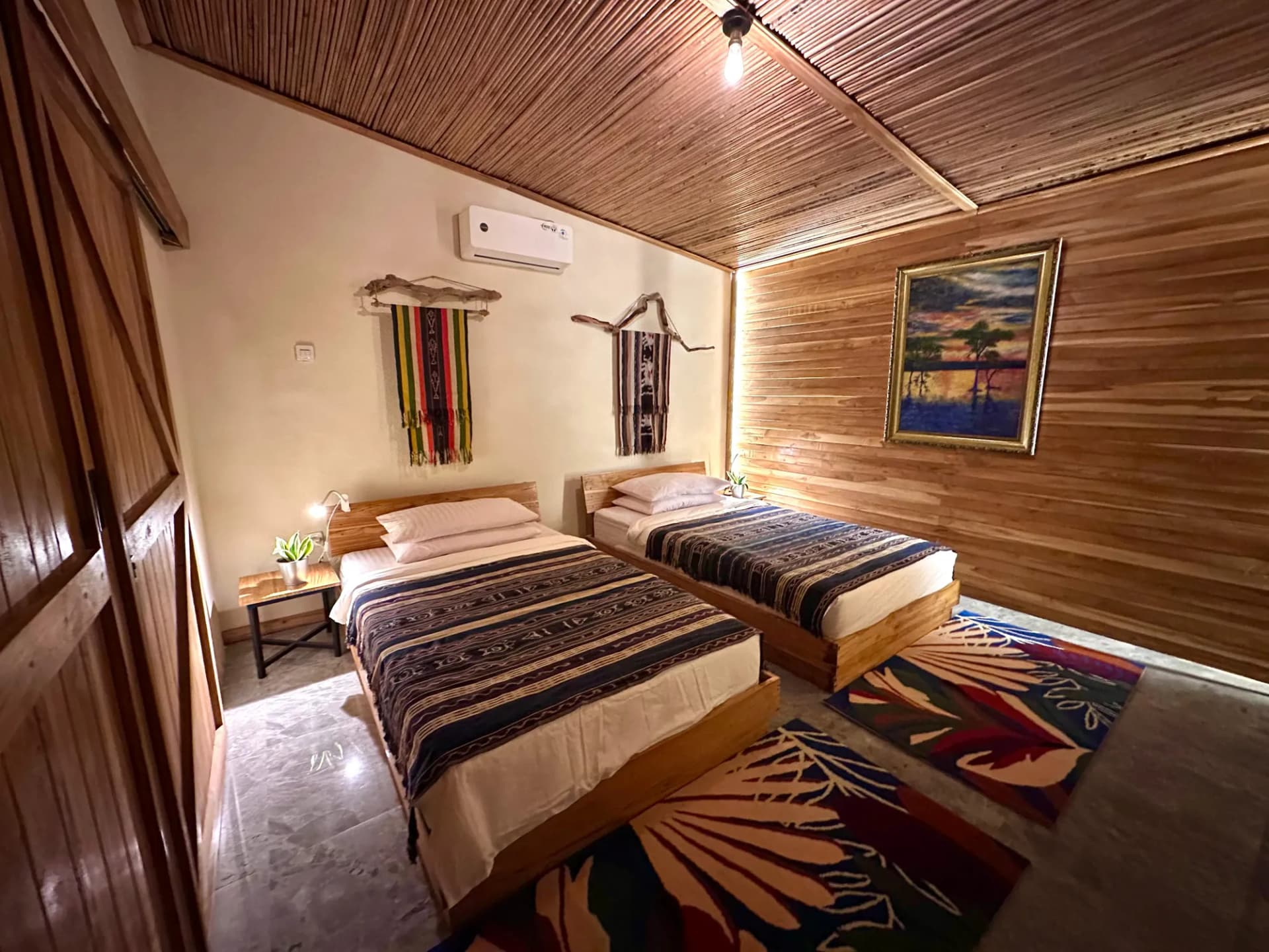 Twin bedroom at Moko Alor Dive Resort with wooden walls and ceiling, patterned bedspreads, woven wall hangings, and geometric floor rugs