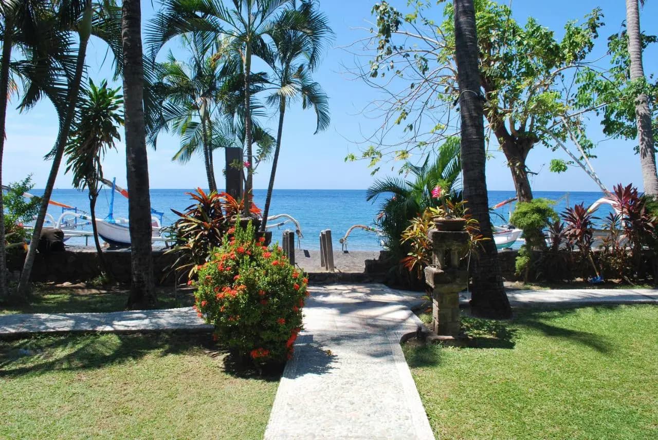 Coral View Villas grounds with palm trees, flowering plants, manicured lawn, stone pathway, and water view beyond