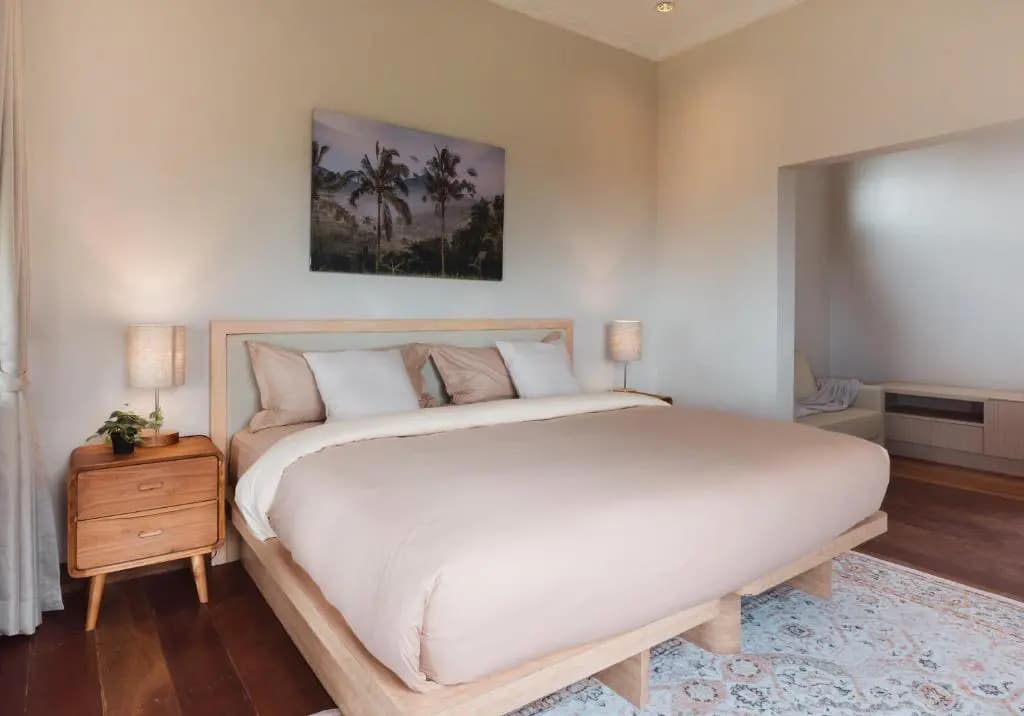 Girihill Farmhouse bedroom with wooden-frame bed, white bedding, wood nightstand with lamp, wooden flooring, and landscape artwork on wall