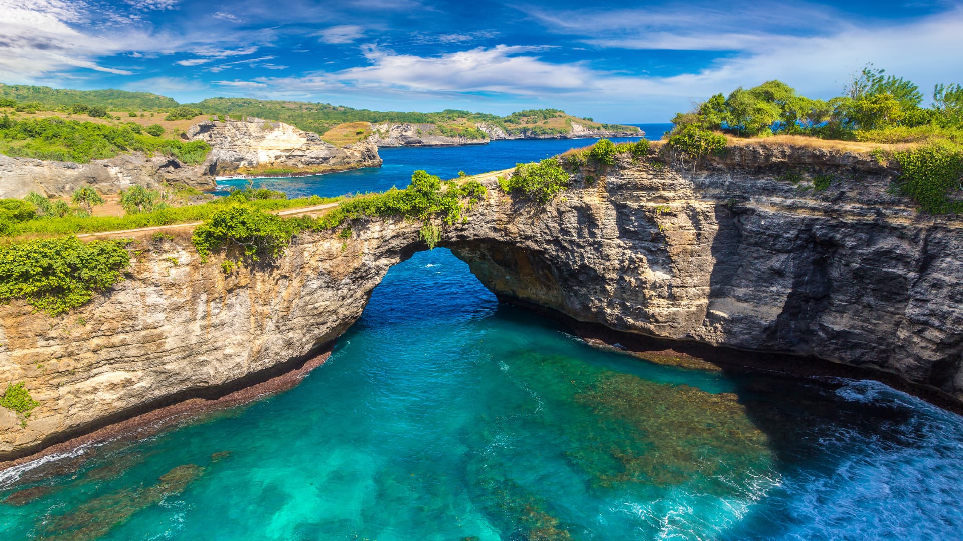 Natural rock arch over turquoise water with a coral-lined lagoon and coastal cliffs in the background