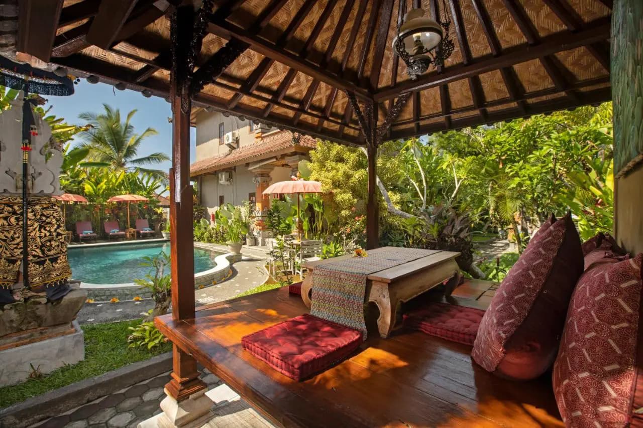Covered wooden pavilion with cushioned seating overlooking a swimming pool and tropical gardens at Umasari Cottage Ubud