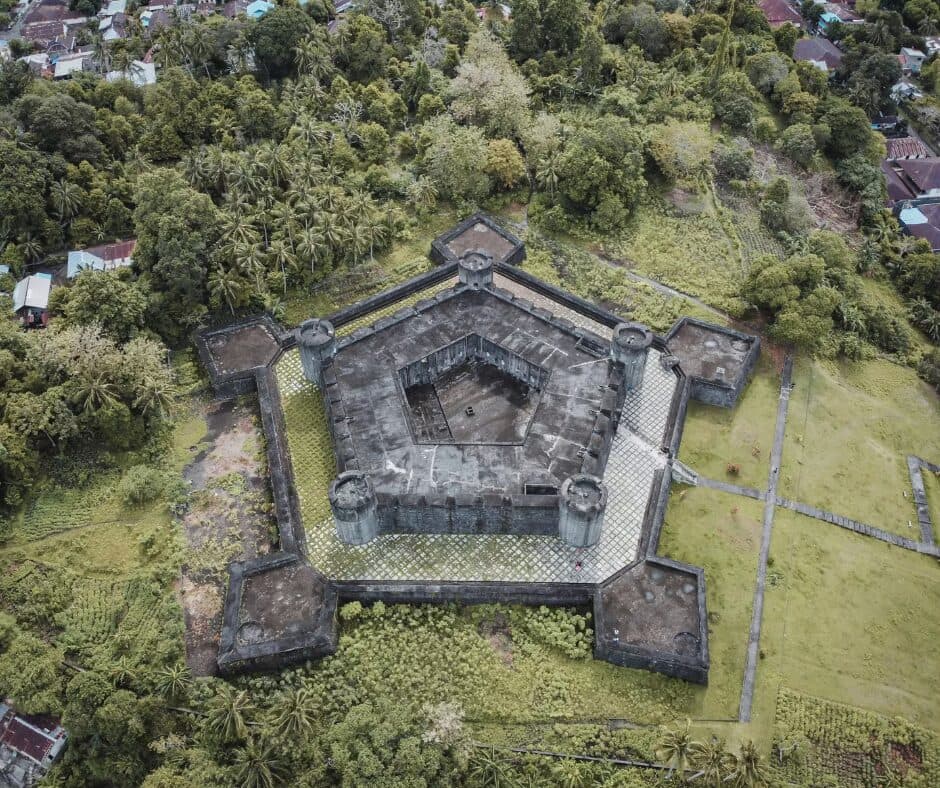 Aerial view of a star-shaped stone fort with a pentagonal courtyard, surrounded by dense green trees and rooftops