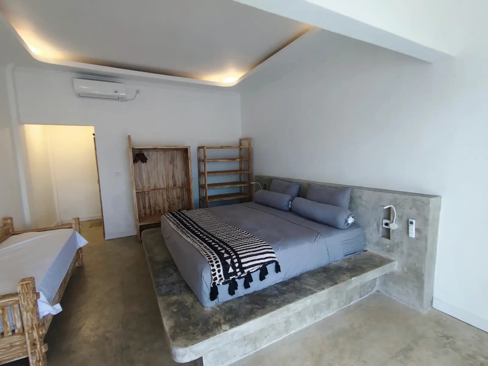 Spacious bedroom at Sanctum Nusa Penida Dive Resort with raised platform bed, concrete headboard, wooden storage, and ceiling lighting