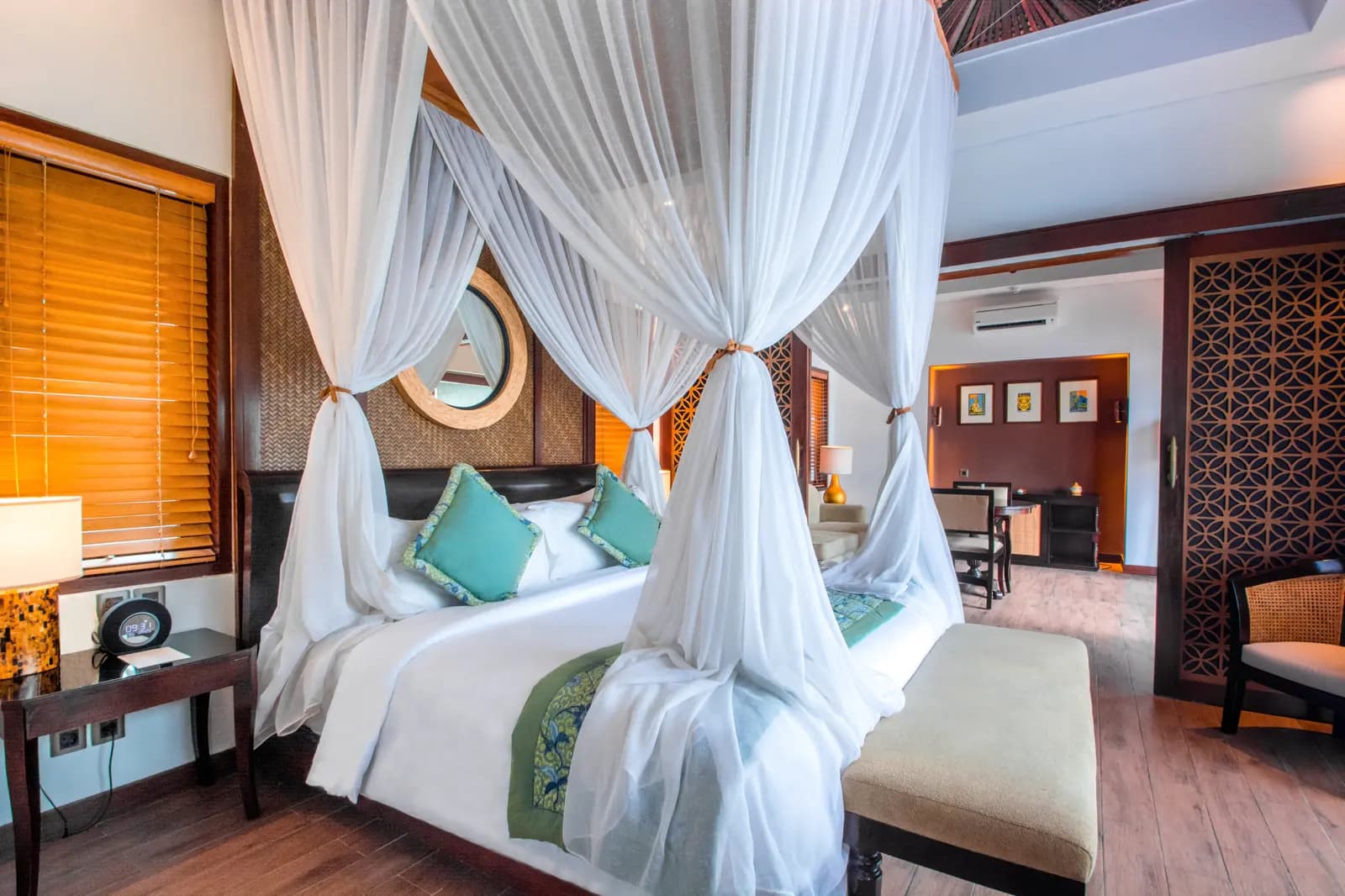 Four-poster bed with white drapes and turquoise cushions in a spacious bedroom at Lembongan Beach Club & Resort, with wooden furnishings and dark accent walls