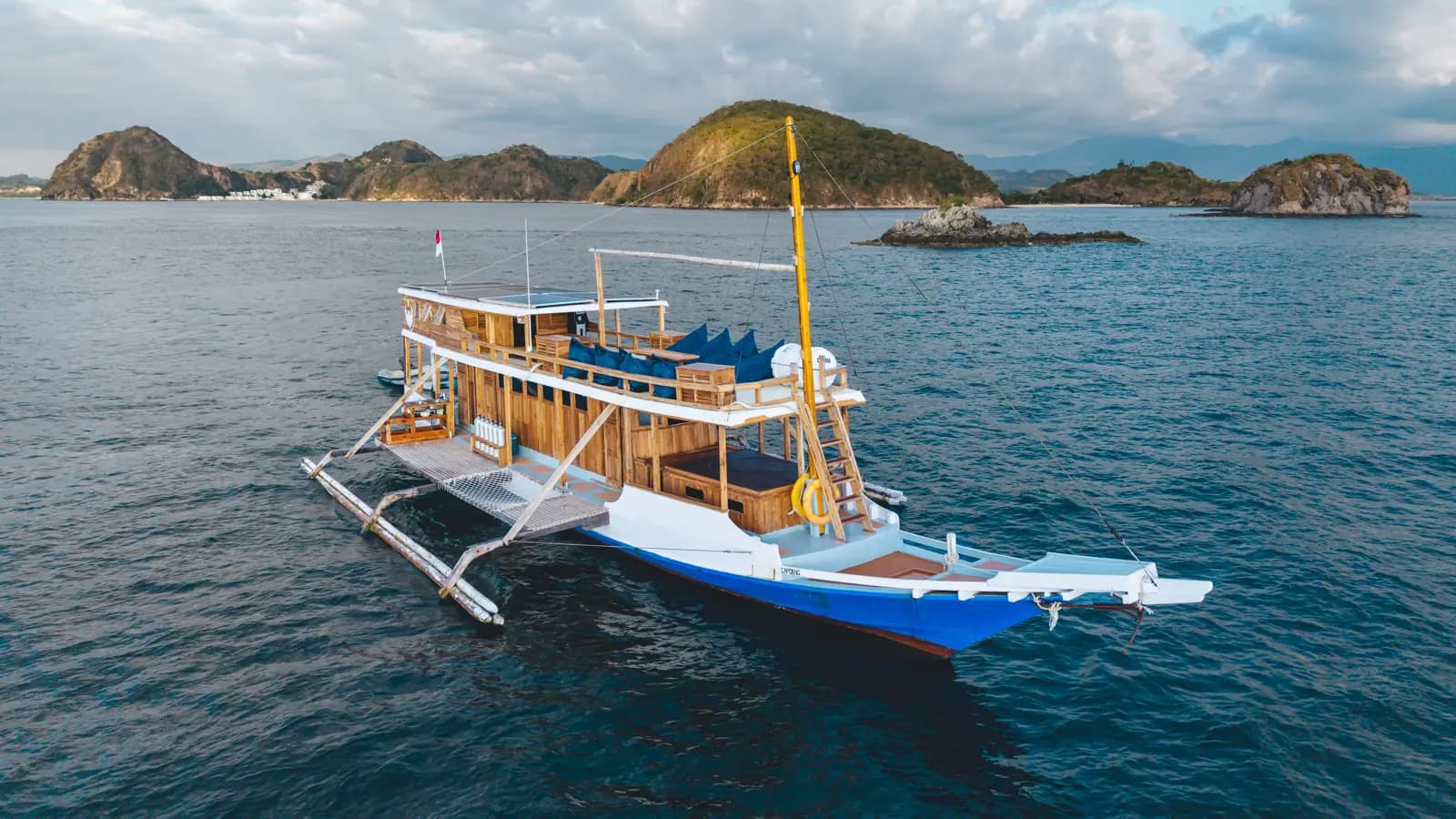 Aerial view of the liveaboard Capoeng anchored near outrigger floats with hills and small islands in the background
