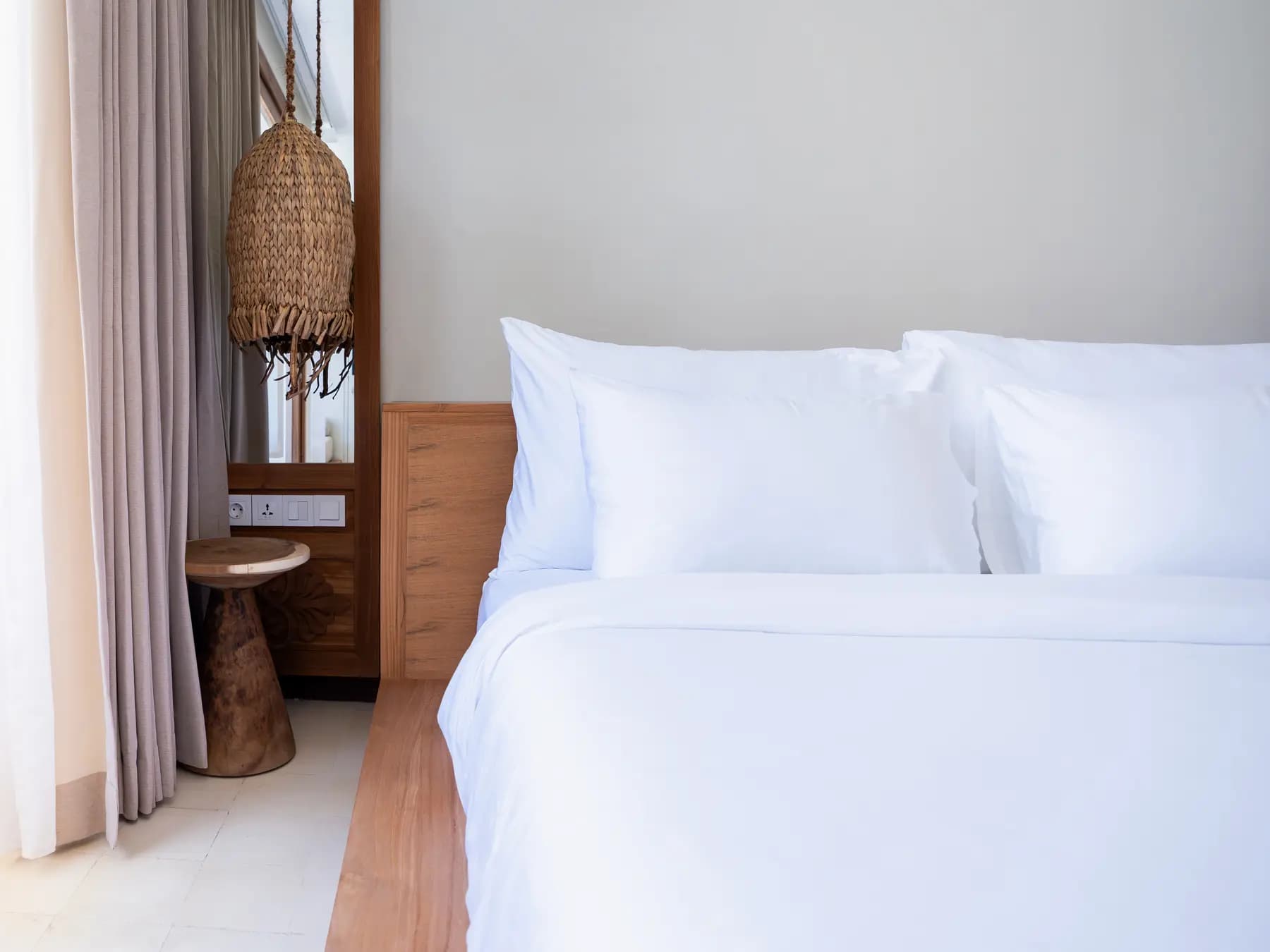 Cocana Resort bedroom with white bedding, wooden bed frame, woven pendant lamp, and curtains