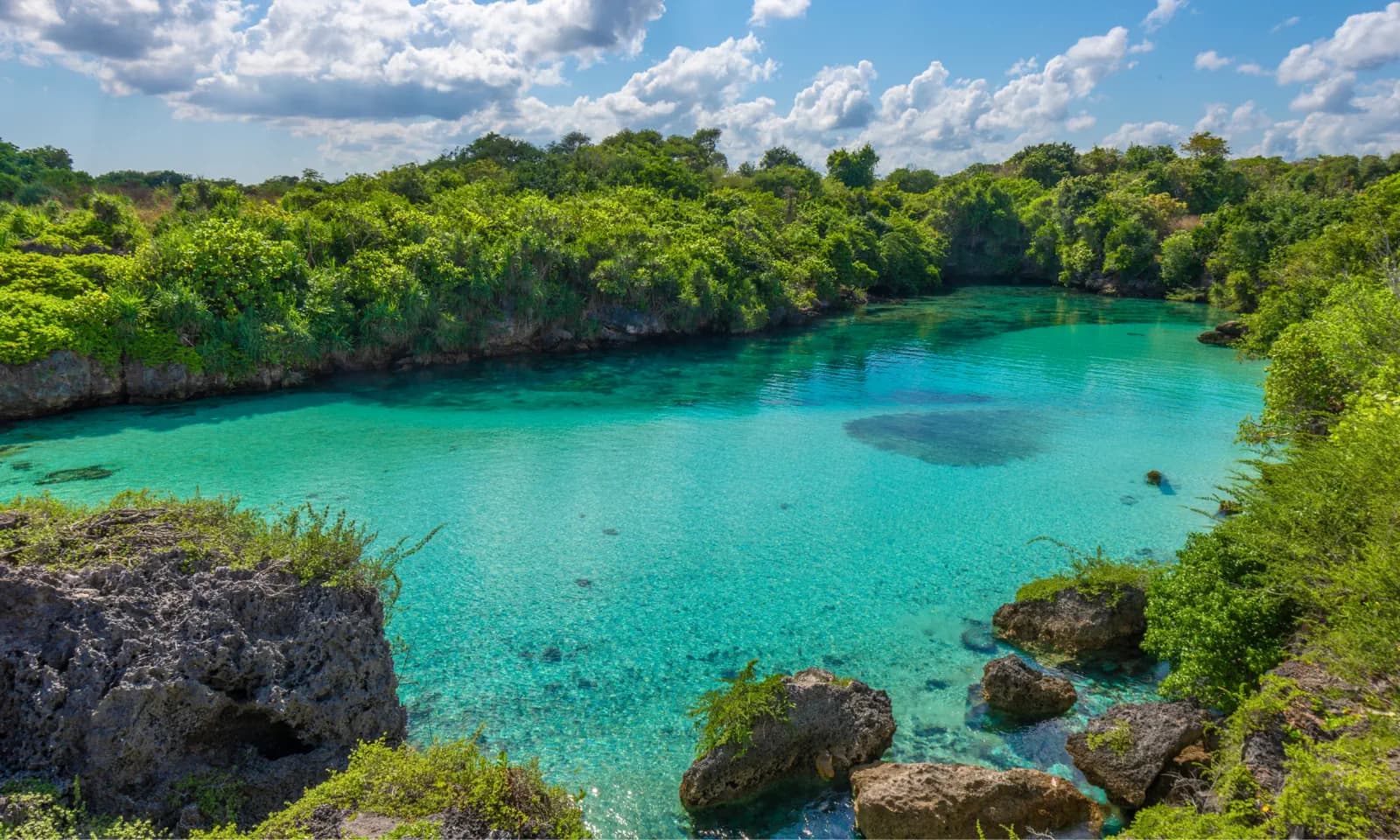 Turquoise lagoon surrounded by limestone rock formations and dense green forest under a partly cloudy sky