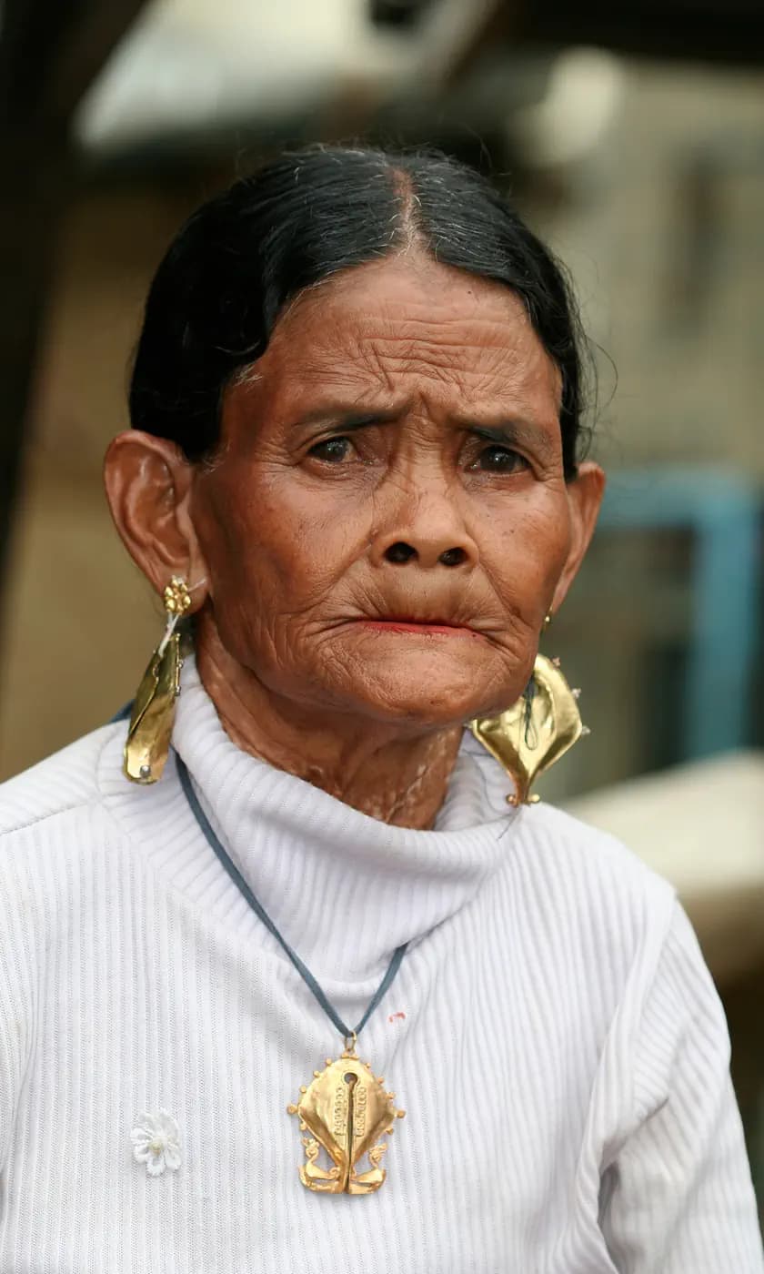 Portrait of a woman wearing large gold earrings, a gold pendant necklace, and a white ribbed sweater
