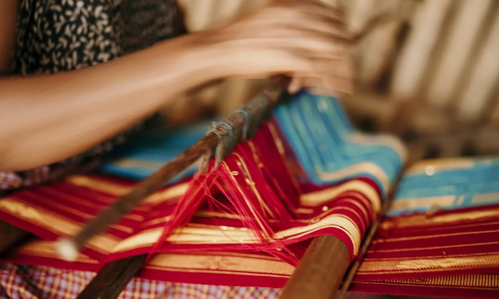 Close-up of hands weaving red, blue and gold threads on a traditional wooden loom