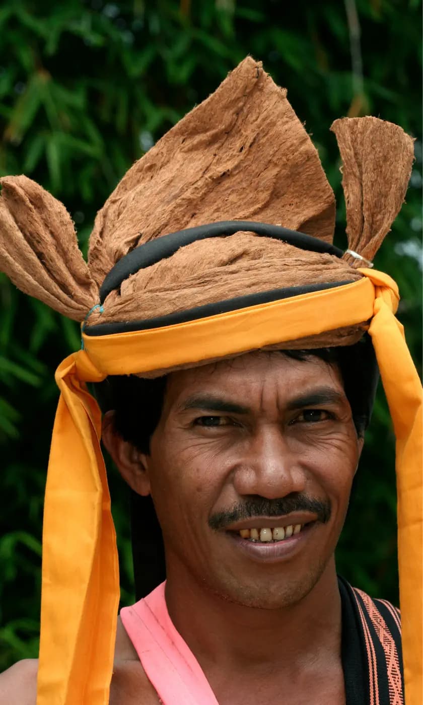 Man wearing a traditional woven headdress with pointed folds, secured by a bright yellow cloth band tied under the chin