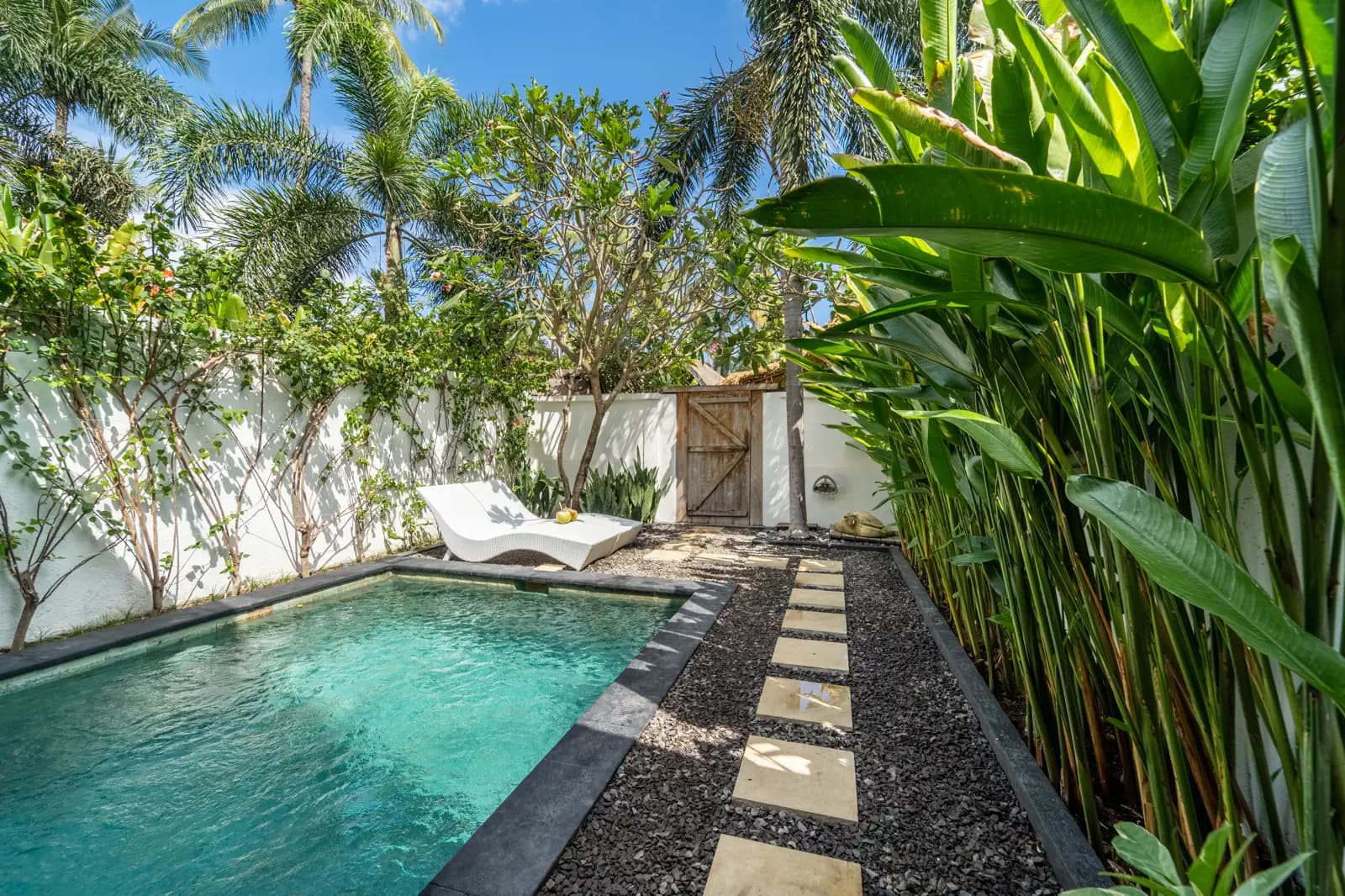 Akasia Villas courtyard with swimming pool, tropical plants, white-walled building, and stone pathway under clear sky