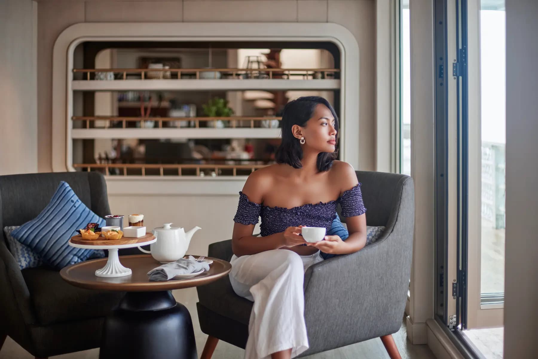 A guest relaxes in a lounge chair aboard Lako Di'a, holding a teacup beside a tiered tray of pastries