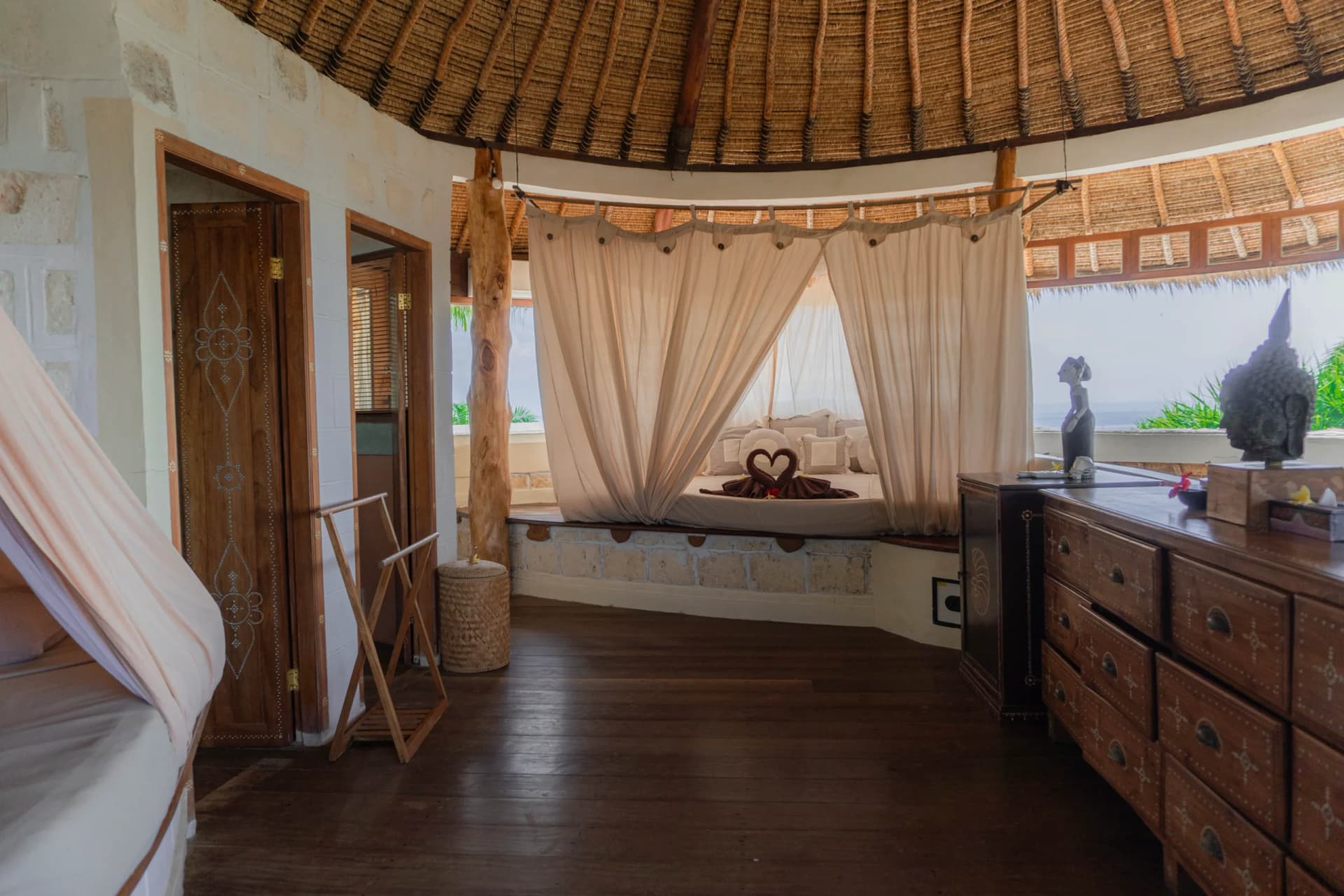 La Joya Resort bedroom with thatched ceiling, wooden furniture, draped window seating area, and view outside