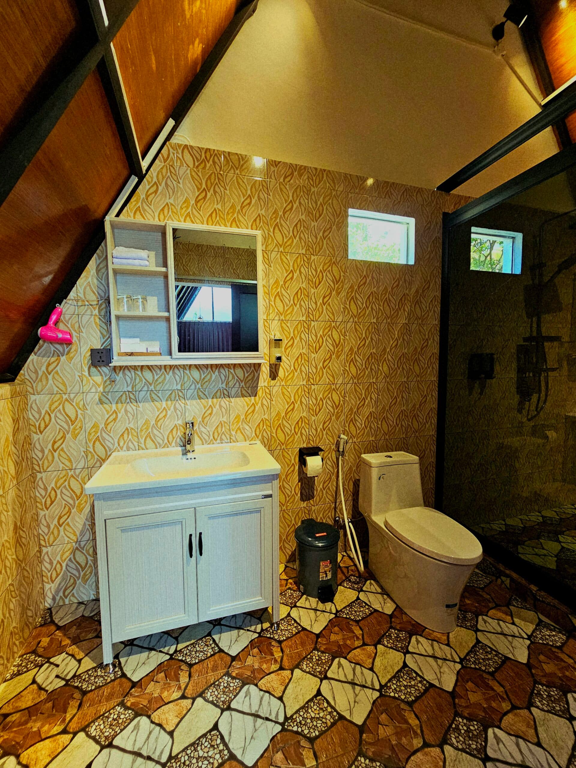 Bathroom with patterned wallpaper, white vanity sink, toilet, shelving unit with mirror, tiled floor, and glass shower enclosure