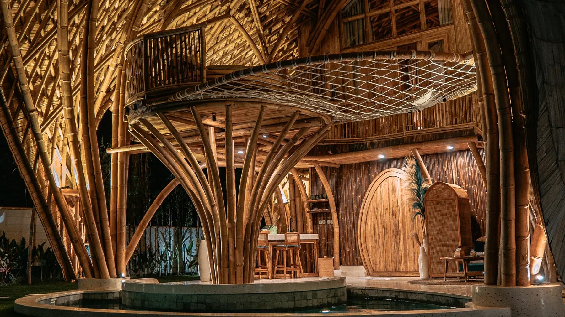 Villa Tokay's wooden interior features curved timber beams, a platform with railings, bar seating, and a water feature in the foreground