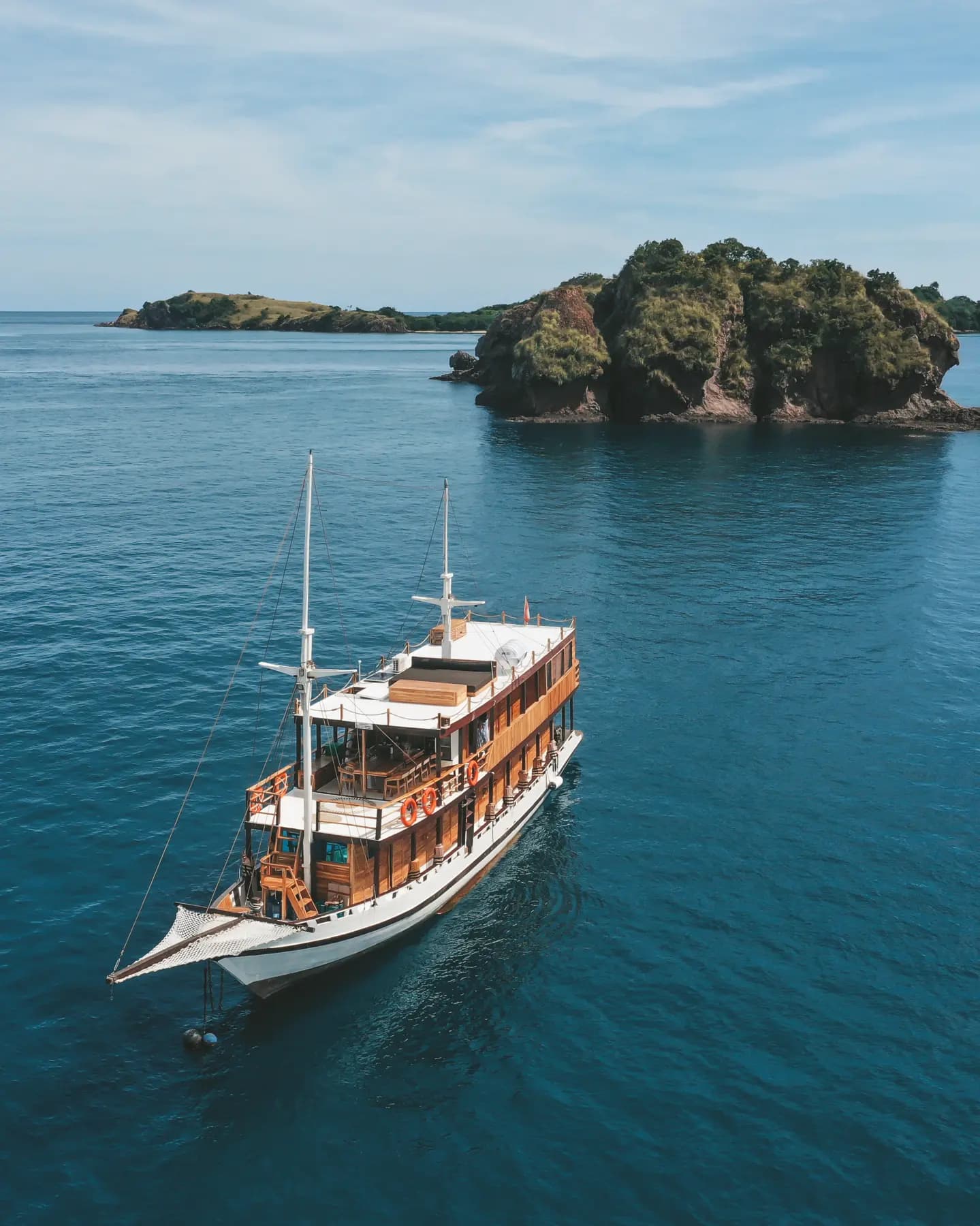 Aerial view of the liveaboard Papiton Duwa anchored near rocky, tree-covered islets in calm blue water