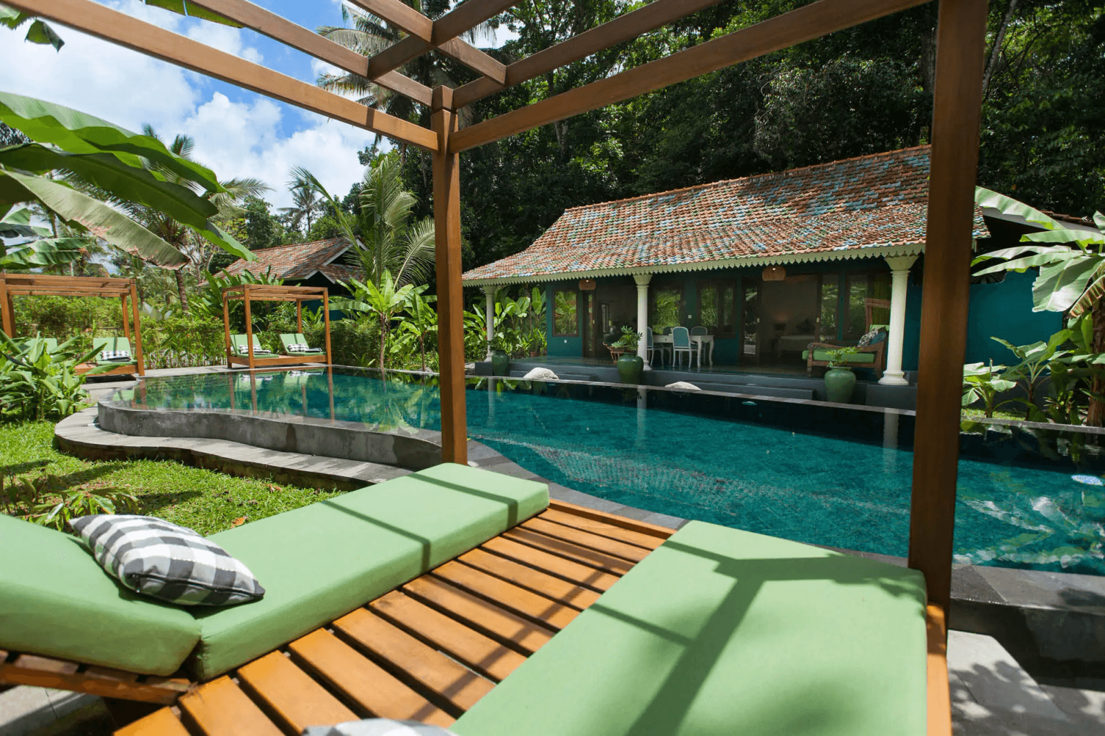 Darmada Eco Resort pool area with wooden pergola, green loungers with pillows, wooden deck, and thatched-roof building with open veranda beyond