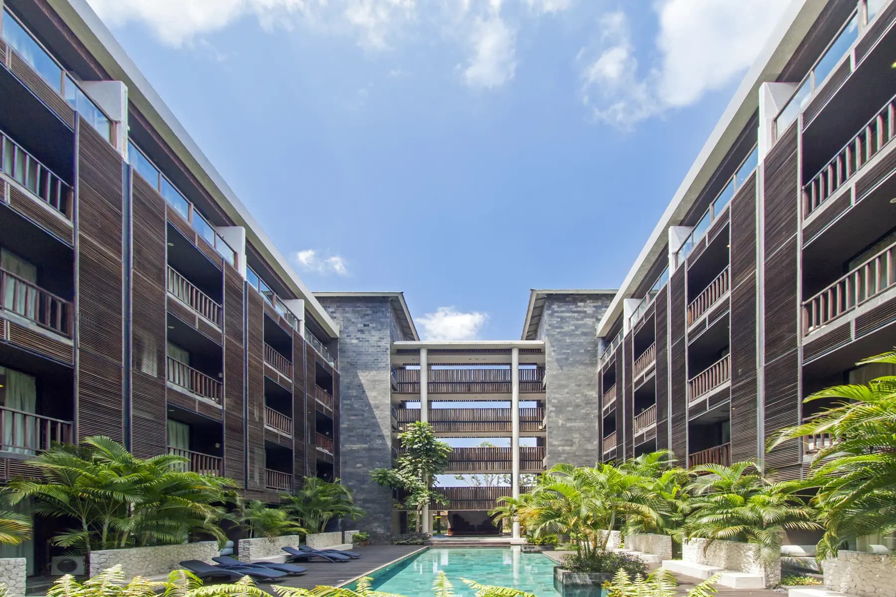 Le Grande Uluwatu courtyard with a central swimming pool, surrounding multi-story residential buildings with balconies, and tropical plants