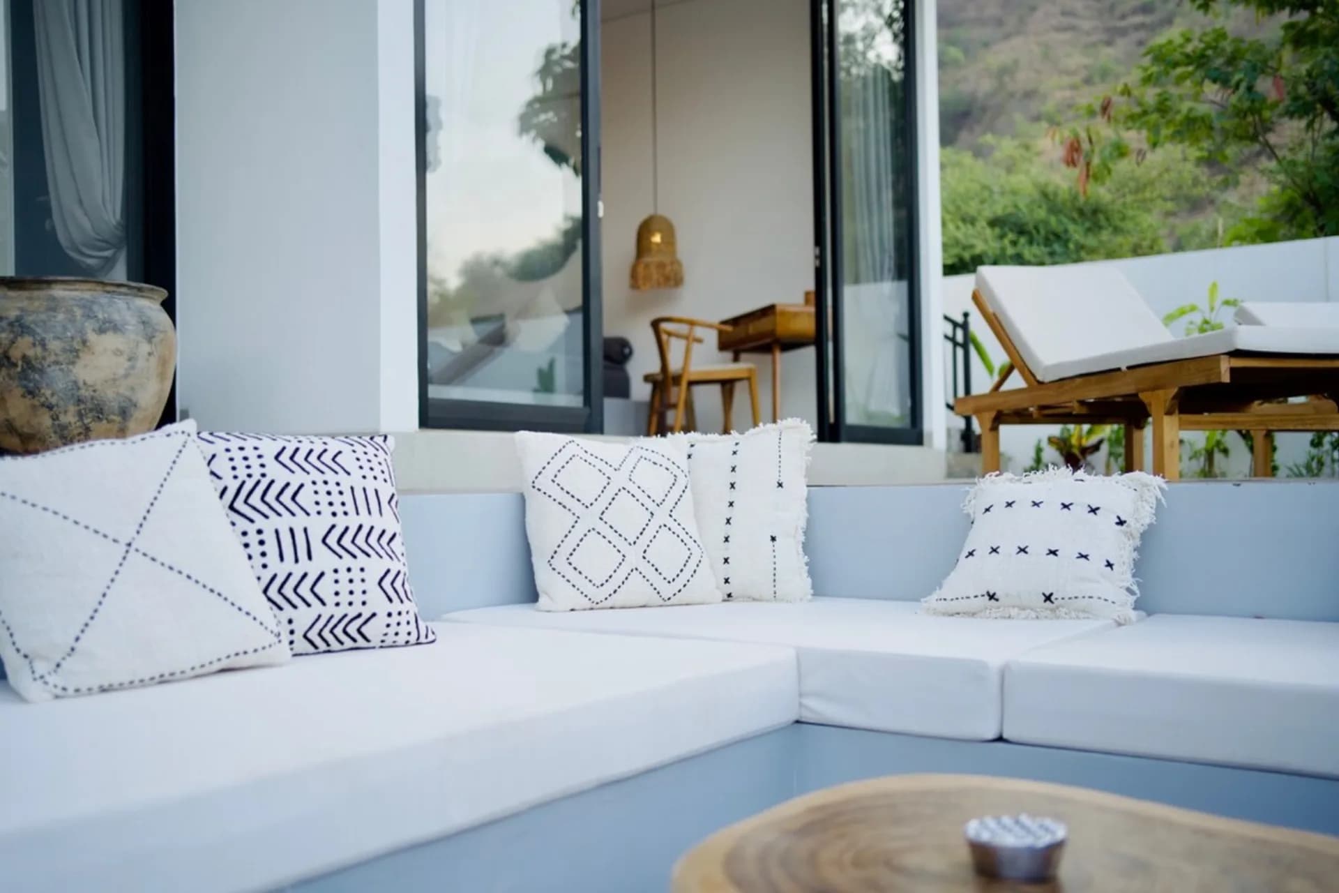 Villa Mercure outdoor seating area with white sectional sofa, patterned cushions, wooden table, and large windows overlooking landscaped grounds