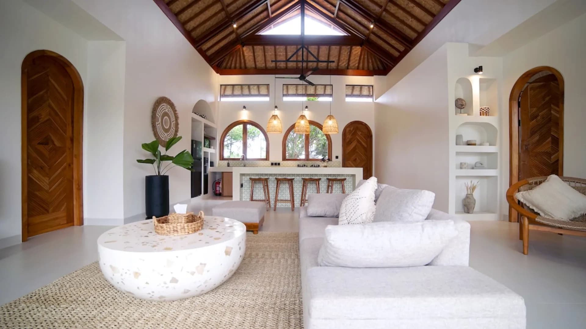 Villa Nagaïa's open-plan living area with white seating, wooden doors, pendant lights, and high vaulted ceiling with wooden beams
